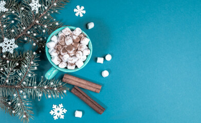 Turquoise Christmas background with fir branches with snow and cup of coffee or cocoa with marshmallows. Top view.