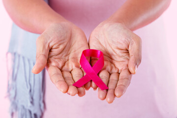 closeup of Woman holding pink ribbon in pullover holding pink ribbon isolated on pink blank copy space studio background,healthcare,medicine concept