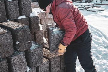a man working as a loader, loads blocks from an arbolite, in the backlight of the sun