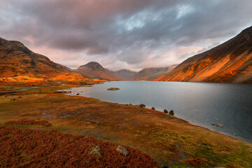 Dramatic view of Wastwater lake and mountains with golden evening light and dark clouds in sky. Lake District, UK.
