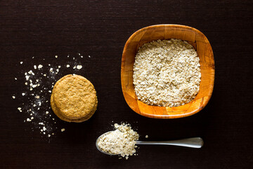 Oatmeal cookies with oatmeal around, bowl and spoon with oatmeal, on wooden background.
