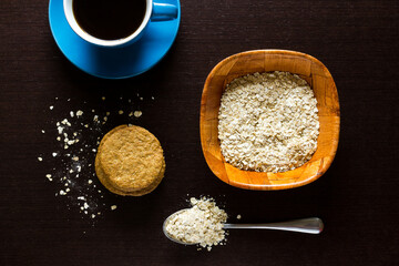 Oatmeal cookies with oatmeal around, oatmeal bowl and blue cup of coffee, on wooden background.