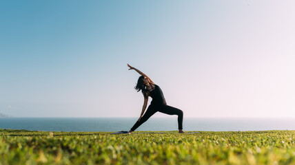 Profesora de yoga practica al aire libre en una tarde soleada con fondo de cielo y mar. - obrazy, fototapety, plakaty