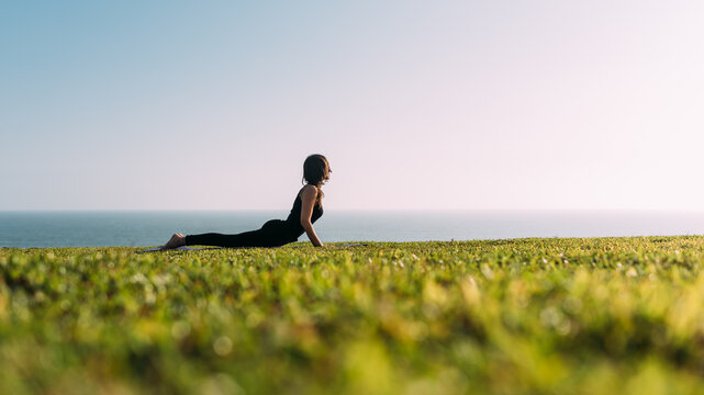 Profesora de yoga concentrada viste de negro practica yoga recostada en el c&eacute;sped al aire libre disfrutando de la tarde.