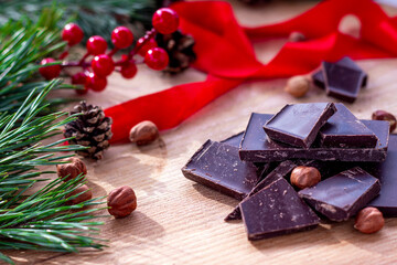 Home made chocolate with Christmas decoration on background. Chocolate, nuts, fir cones and branch, red berries and wrapping tape.  