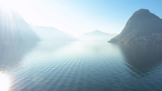 Aerial view of Lugano lake with Melide bridge on background. Dolly in of aerial shoot with drone in Switzerland. Close up of wave&rsquo;s water.
