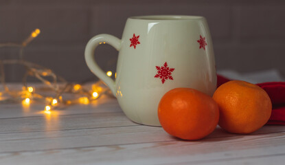 Obraz na płótnie Canvas Winter holiday. Christmas cup with yellow lights and tangerines on wooden table.