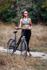 Fototapeta na wymiar Fit young woman wearing sportswear standing with her bicycle on blurry autumn background