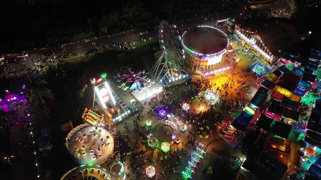 Amusement park with a lots of people and rides that spin and glow at night with neon lights