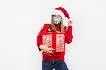 Attractive young woman in christmas santa claus hat, wearing a medical protective mask on her face, with a gift box on a white background