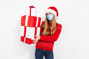 Young happy woman in Christmas Santa Claus hat, in a medical mask on her face, with Christmas gifts, on a white background, Santa's helper