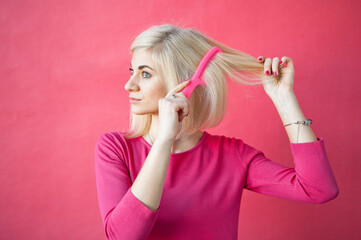 Excited blonde girl in winter blue set sitting on floor among colorful shopping bags over pink background, raising hands in emotional gesture, copy space