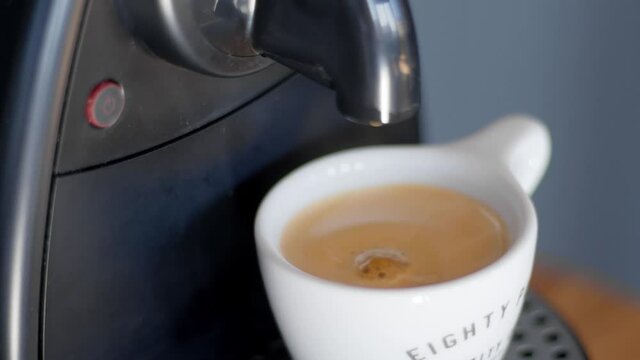 Closeup making coffee from a capsule in an automated Nespresso machine. Coffee drops. White ceramic cup. Black coffee maker. High quality video 4k footage. 