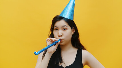 Funny asian woman with party hat blowing into the whistle . Party and celebration concept. High...