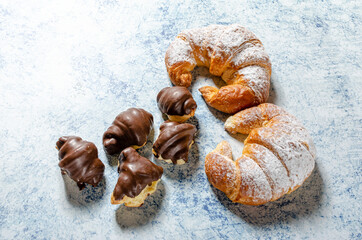 Two freshly baked croissants with glass sugar and several mini chocolate croissants on a blue background with texture.