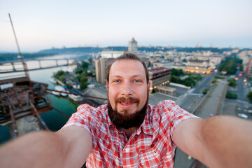 Roofer, a bearded man, takes a selfie on the rooftop. In the background is a panorama of the...