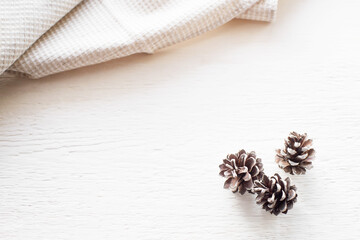 Christmas background. White kitchen towel or cloth napkin and three pine cones on a white wooden table. Top view with copy space