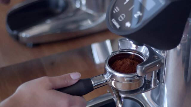 Caucasian white woman's barista hand inserting double porta filter in the grinder to collect ground specialty coffee beans for making espresso. Professional grinder. High quality 4k video footage.