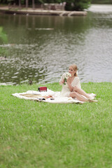 A young girl in a white dress with white flowers in her hands. By the lake on a sunny summer day.