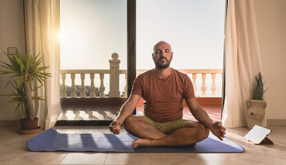 Young man doing meditation at home with digital tablet - Sunset in background