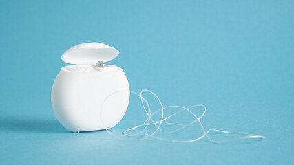 Container with dental floss. Floss on blue background. White dental floss case isolated. Open dental floss container