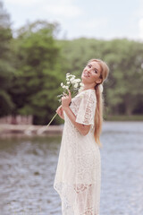 A young girl in a white dress with white flowers in her hands. By the lake on a sunny summer day.