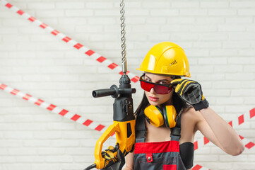 a woman in a hard hat and overalls with a puncher on the background of a white textured brick wall