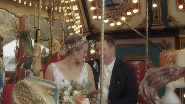 A newlywed couple laugh, kiss, and pose on a carousel