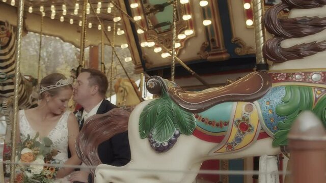A groom kisses his bride on the forehead while sitting on a carousel