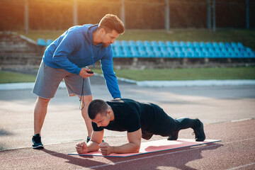 man doing plank exercise and workout with personal fitness trainer outdoor