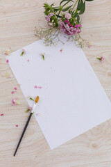 White paper with paintbrush, flowers and petals on wooden background