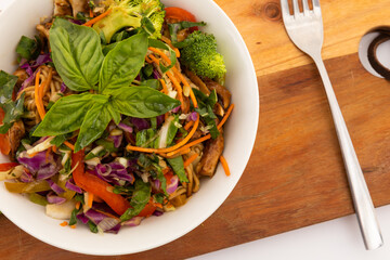 High angle view of bowl with salad and basil leaves on wooden board