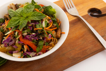 High angle view of bowl with salad and basil leaves on wooden board
