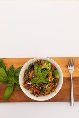 High angle view of bowl with salad and basil leaves on board on white background
