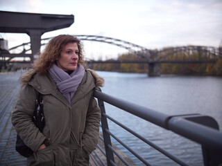 Woman deep in thought, stops next to a river and stares into distance. City Frankfurt am Main during autumn.