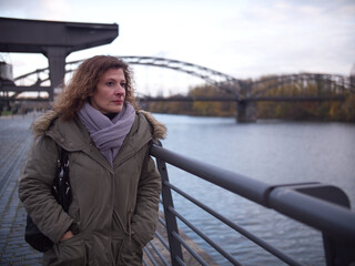Obraz premium Woman deep in thought, stops next to a river and stares into distance. City Frankfurt am Main during autumn.