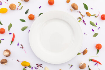 White plate surrounded by fresh vegetables on white background