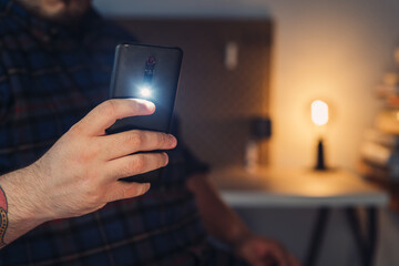 Closeup shot of a man's hand taking a picture with a turned on mobile phone camera flashlight