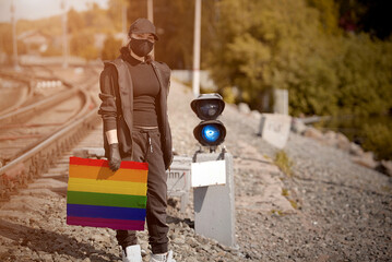 a young activist with an LGBT flag poster in her hand on the railway tracks, dressed in black clothes