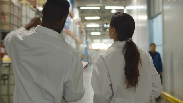 Back view of african and caucasian engineers in lab coats examining industrial warehouse