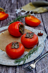 Still life of ripe orange persimmon and rosemary sprigs on a silver platter.