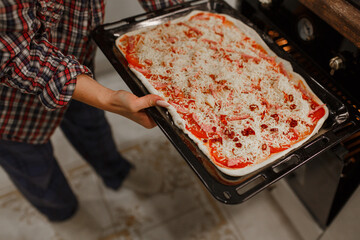 hands holding a baking sheet with pizza