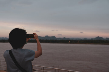 Obraz premium rear view of woman using smartphone to shoot picture of mekong river during vacation