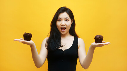 Young excited asian woman holding chocolate muffins in outstretched hands. High quality photo