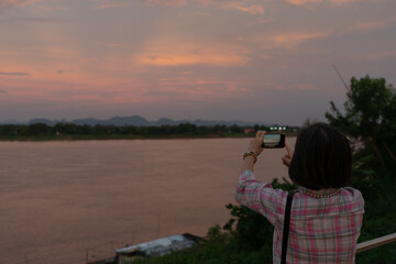 Fototapeta na wymiar rear view of woman using smartphone to shoot picture of mekong river during vacation