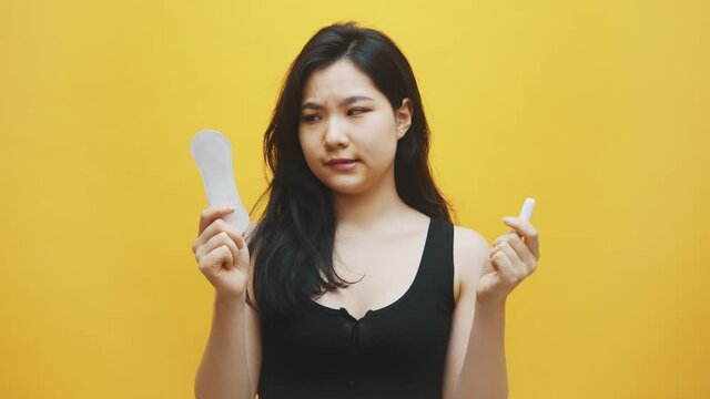 Young unhappy asian woman suffering from PMS. Choice between sanitary pads and tampons. High quality 4k footage