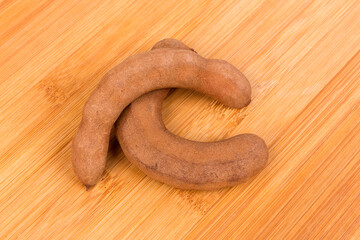 Two pieces dried brown tamarind pods isolated over wood