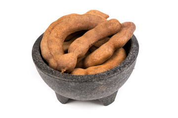 Dried brown tamarind pods in a black bowl isolated over white
