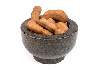 Dried brown tamarind pods in a mortar isolated over white
