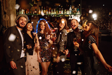 Happy friends throwing confetti and jumping while enjoying party. Group of  young people celebrating together winter holiday. Confetti is fun. Party, celebration, drink, birthday concept.